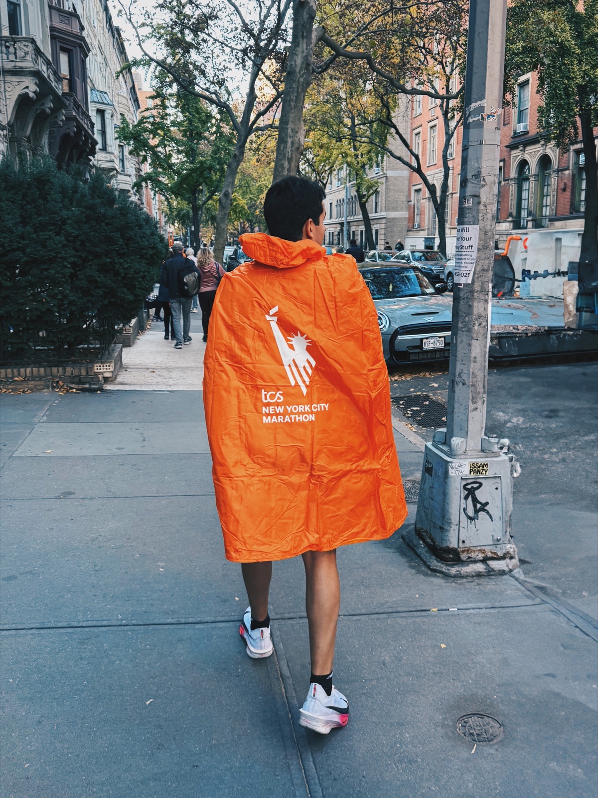Leonardo de costas, com a capa laranja da Maratona de Nova York, caminhando pela rua