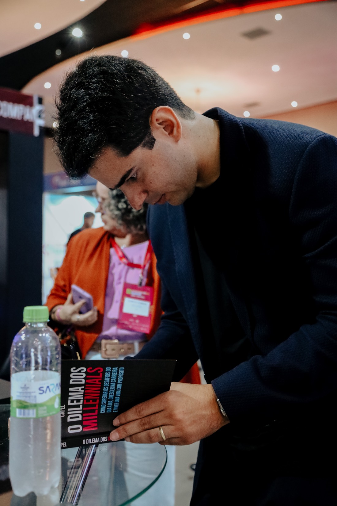 Leonardo Capel curvado sobre uma mesa, autografando um exemplar de O Dilema dos Millennials durante um evento