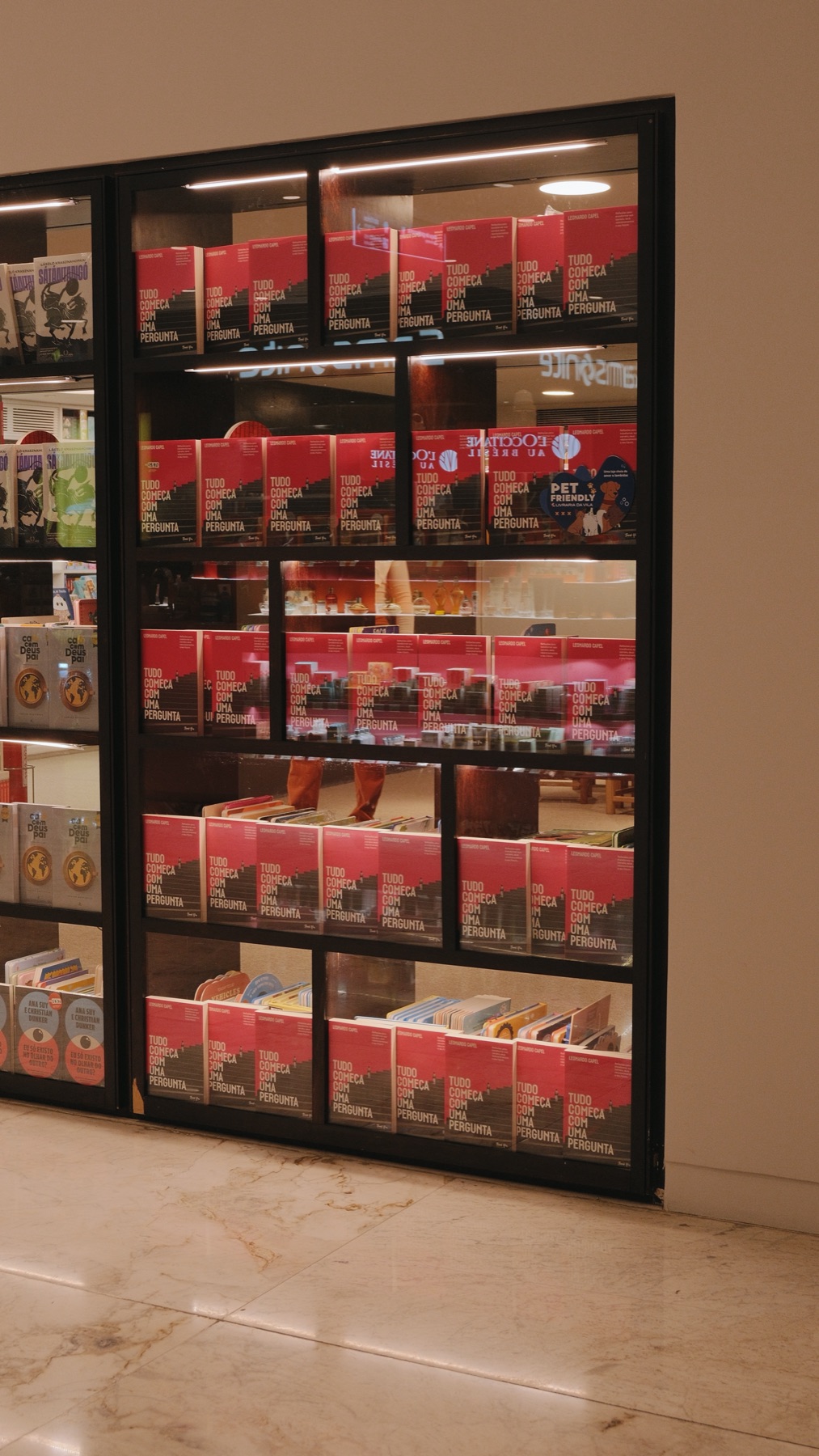 Vitrine de livraria com prateleiras cheias de exemplares de Tudo Começa Com Uma Pergunta